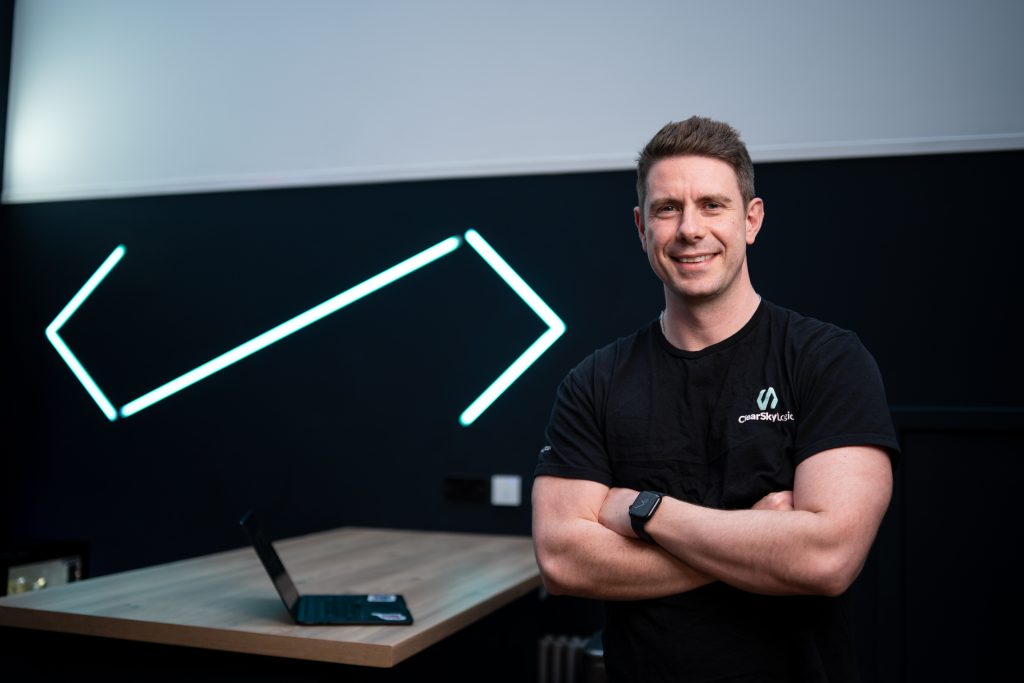 Darren Auld, CEO of ClearSky Logic, standing arms folded in a ClearSky Logic t-shirt in the office