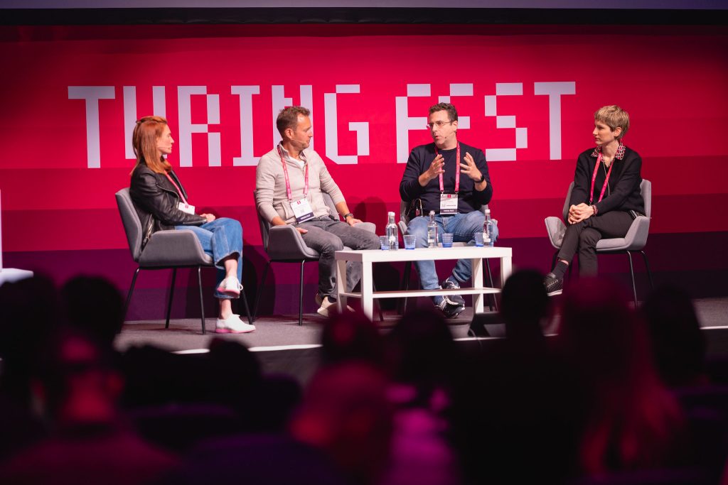 Four panellists seated on stage in front of a Turing Fest backdrop